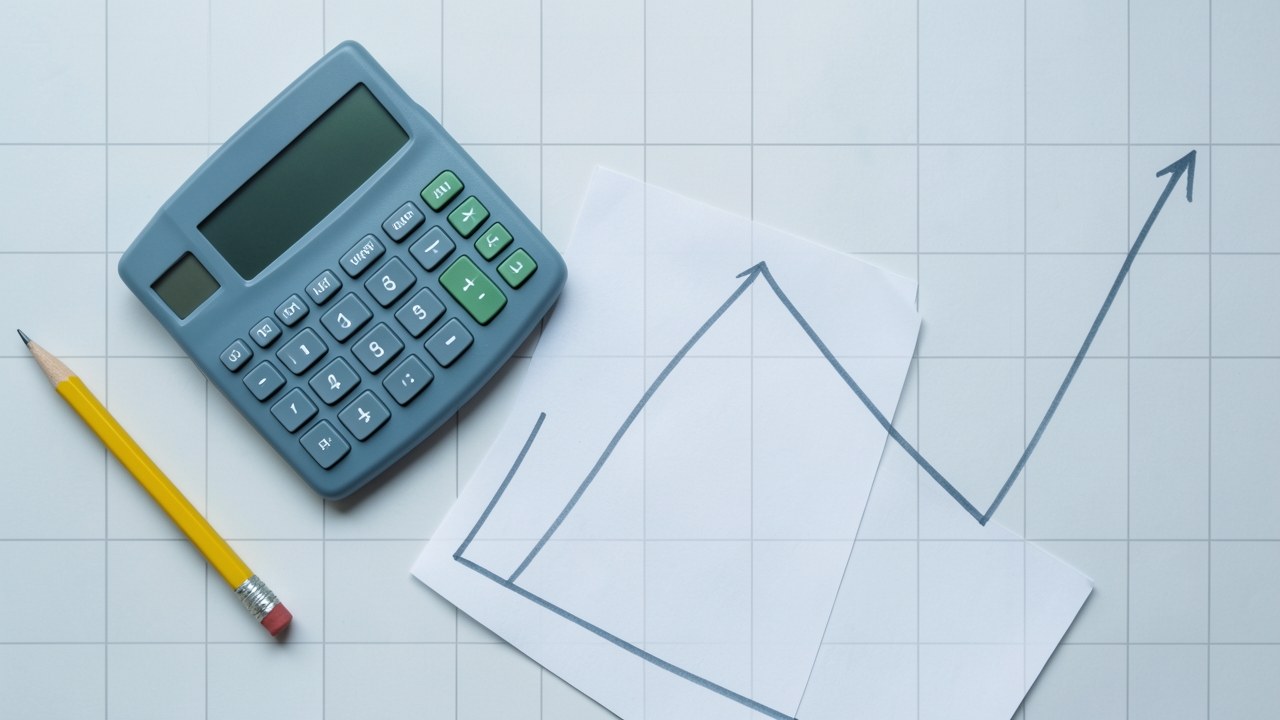 A clean desk with a calculator, a pencil, and a paper showing a simple line chart with an upward trend, set against a background of faint technical grid lines.